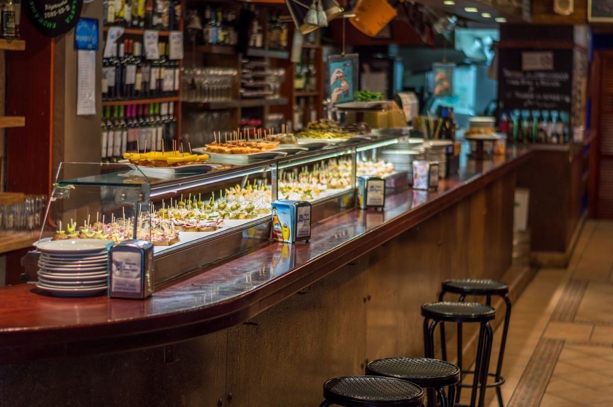 Bancone di tapas con pinchos esposti in vetrina e sgabelli in un bar