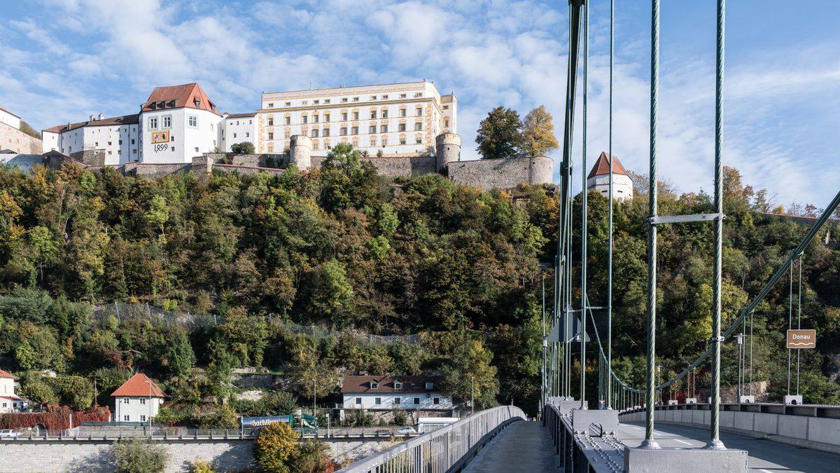 Castello su collina boscosa visto da un ponte sospeso con case ai piedi del pendio