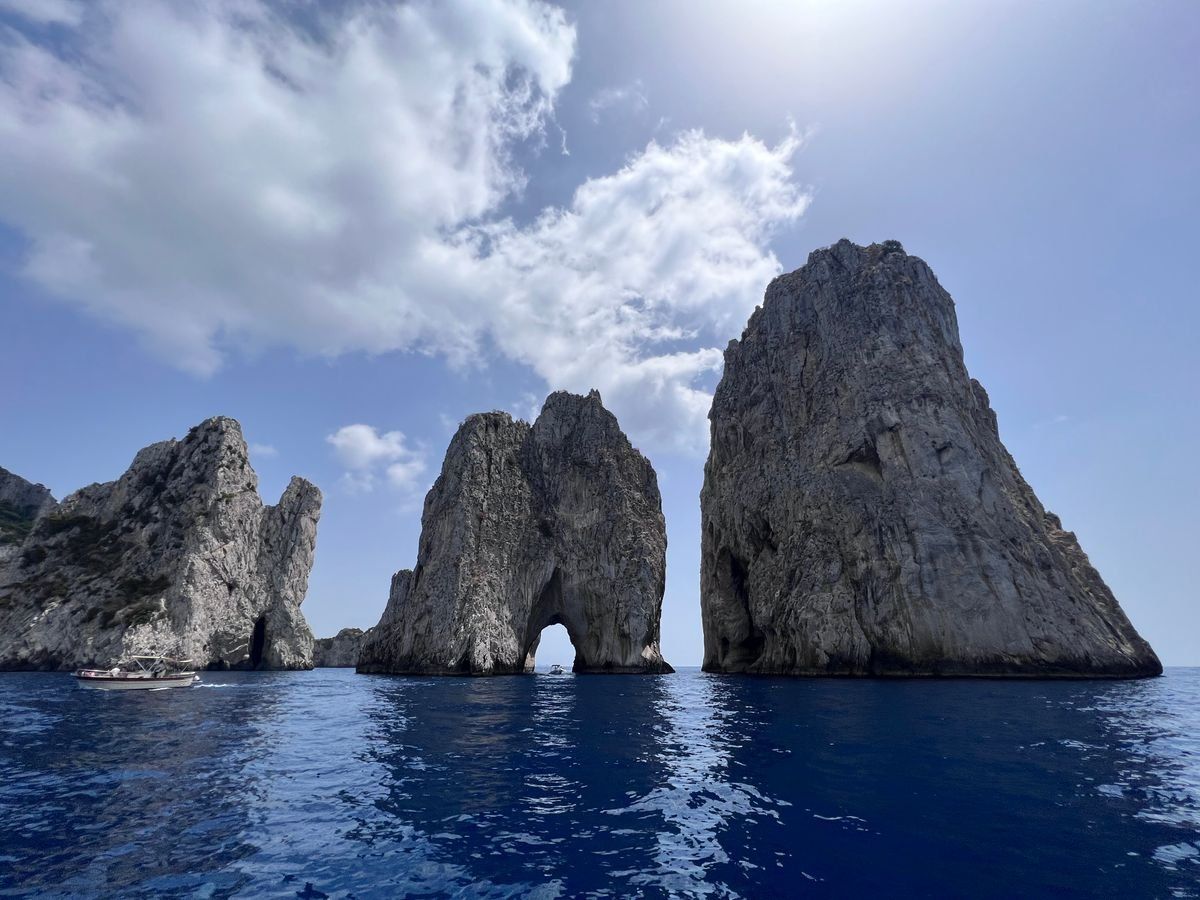 Faraglioni di Capri sul mare blu sotto un cielo con grandi nuvole bianche