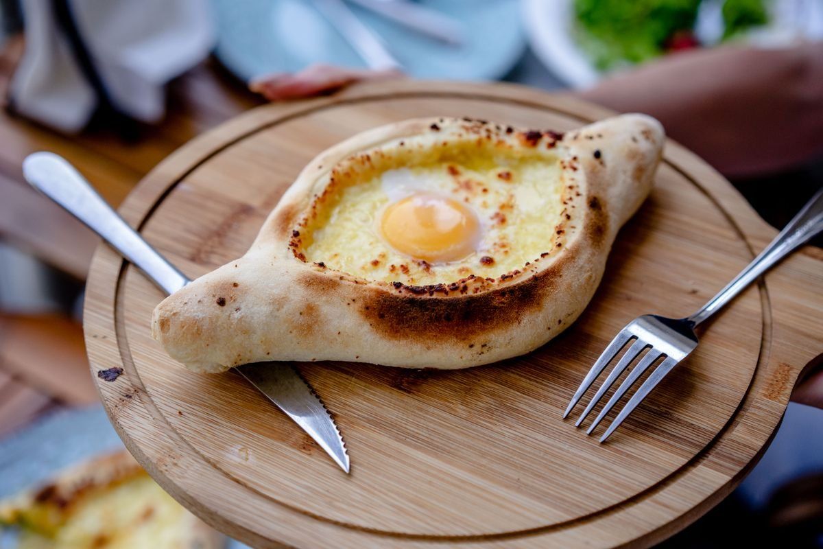 Khachapuri a barchetta con uovo servito su tagliere di legno con posate
