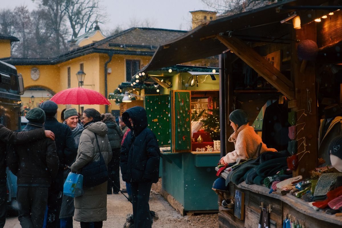 Persone tra le bancarelle di un mercatino invernale sotto una leggera nevicata