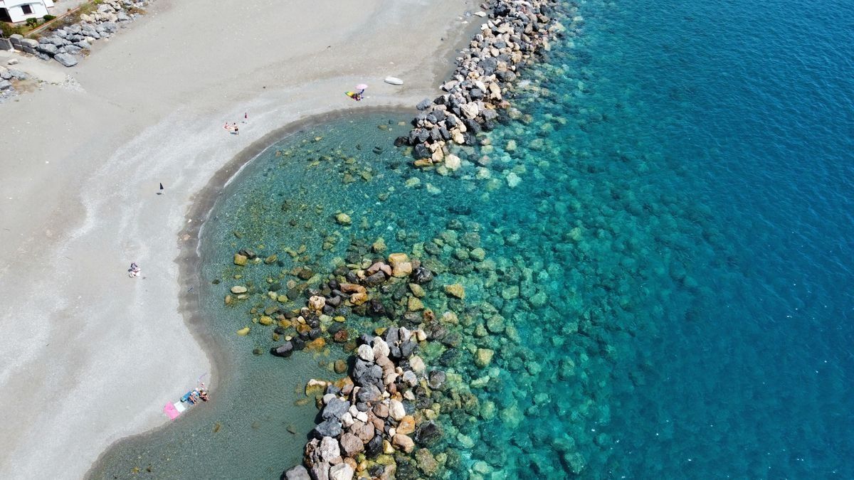 Piccola baia vista dall’alto con spiaggia chiara, scogliera frangiflutti e acqua trasparente