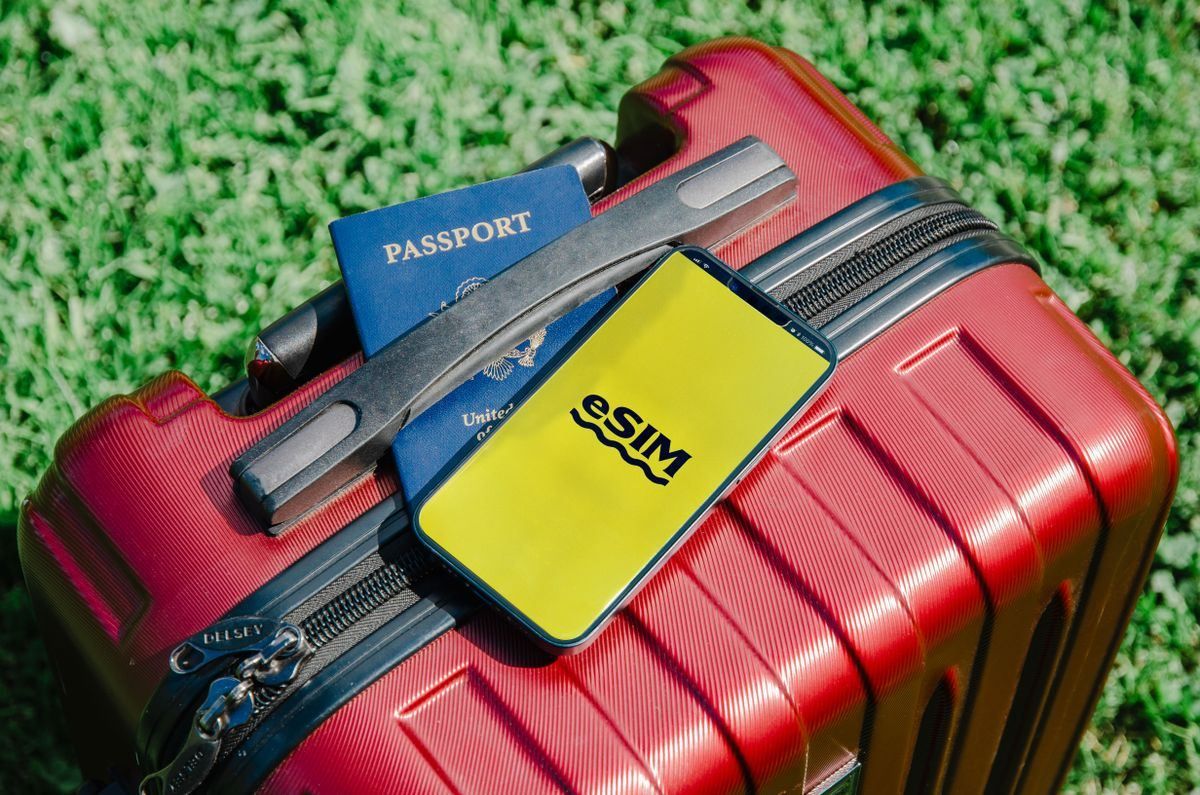 Smartphone con scritta eSIM e passaporto appoggiati su una valigia rossa