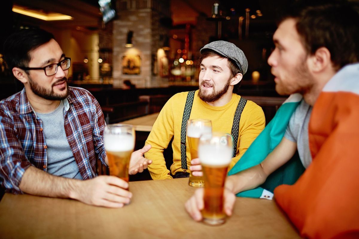 Tre uomini seduti al tavolo in pub con pinte di birra mentre parlano