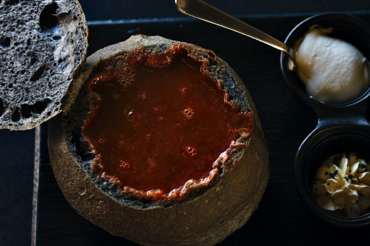 Zuppa rossa servita in una pagnotta scavata con pane accanto e burro in ciotoline