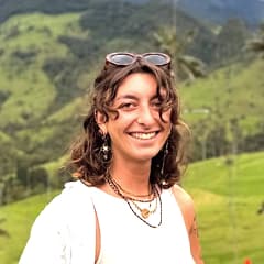 Donna con capelli ricci e occhiali da sole sulla testa sorride, con colline verdi sullo sfondo.
