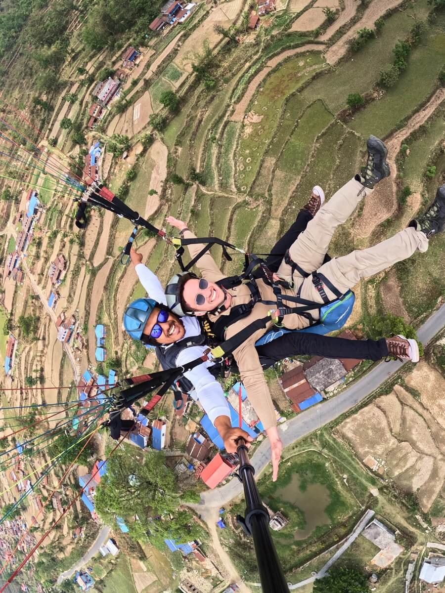 Selfie en parapente tándem desde el aire sobre campos verdes en terrazas y aldeas rurales.
