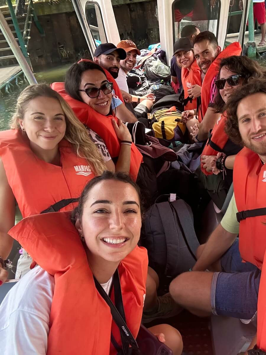 Selfie de un viaje en grupo WeRoad: viajeros con chalecos salvavidas naranjas en un barco con equipaje detrás.
