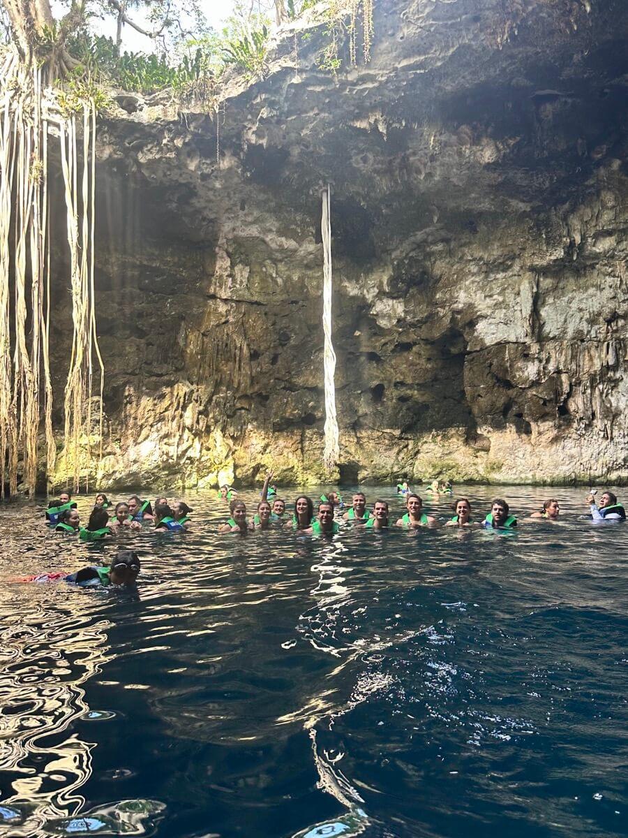Un voyage de groupe WeRoad nage avec des gilets verts dans un cénote naturel entre des parois rocheuses et des cascades.