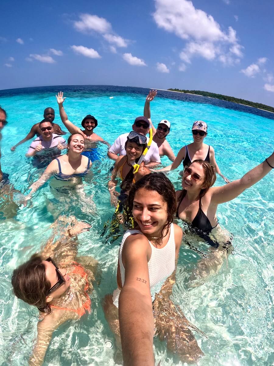 Selfie d'un voyage de groupe WeRoad : voyageurs nageant et faisant du snorkeling dans une eau turquoise sous un ciel bleu.