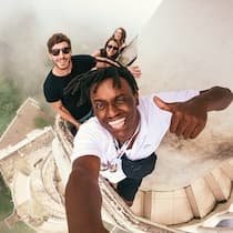 A WeRoad group trip selfie of three travelers atop a curved sandstone structure giving a thumbs-up.