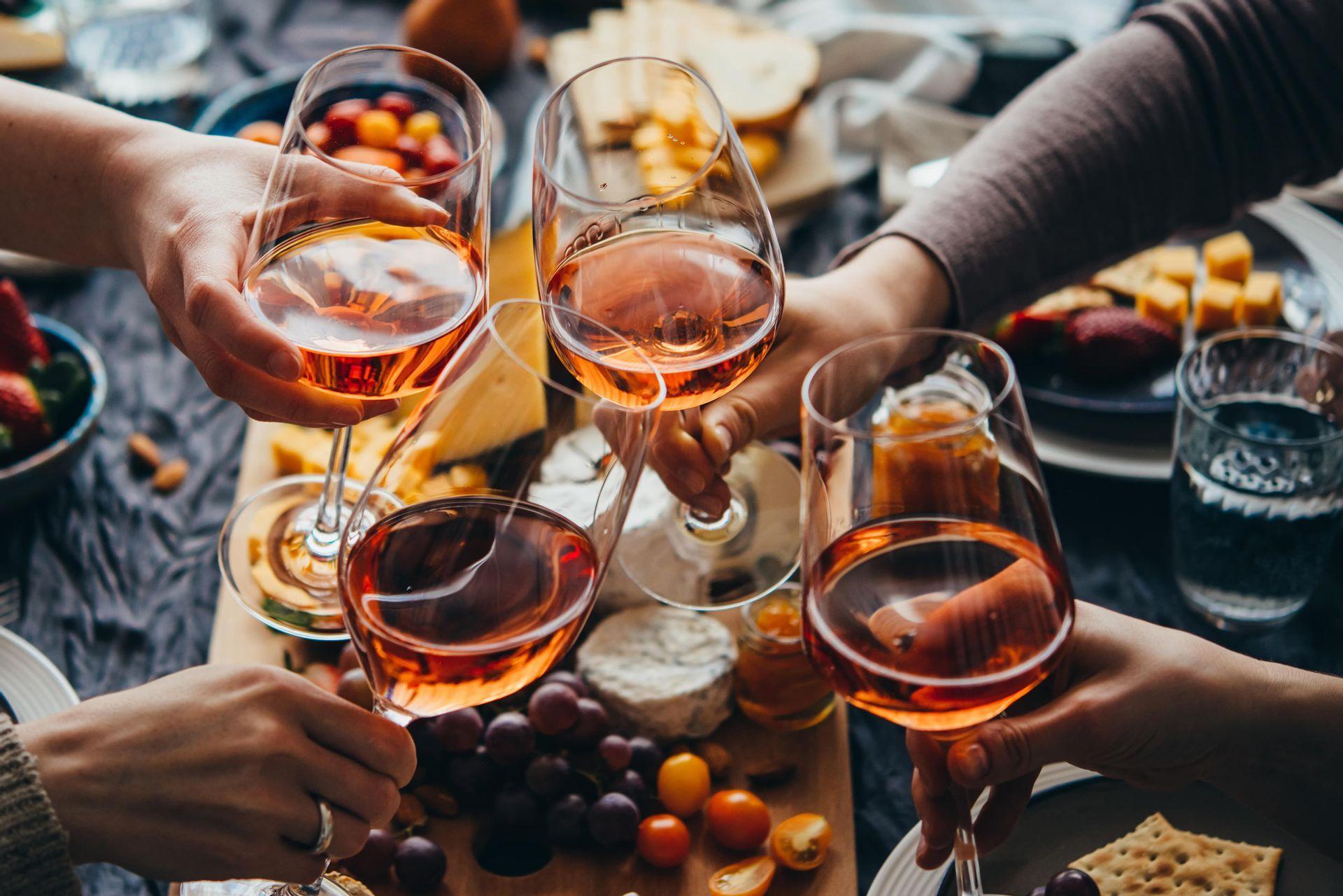 A WeRoad group trip toasting with glasses of rosé wine over a table laden with cheese, fruit, and crackers.