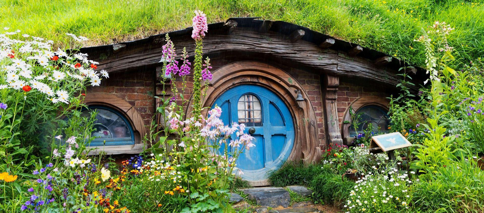 Una casa in stile hobbit, con una porta blu rotonda, incastonata in una collina erbosa e circondata da un lussureggiante giardino di fiori colorati.