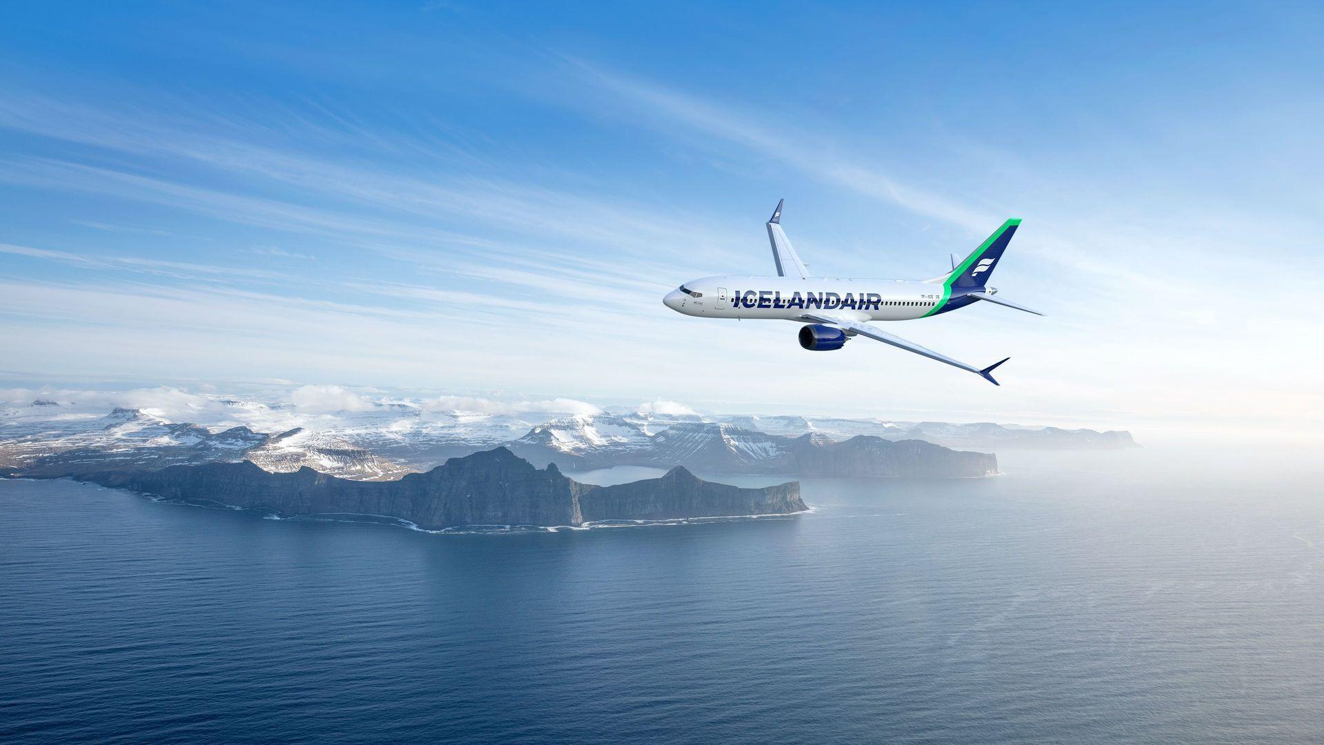Un avion Icelandair survole un paysage côtier avec des montagnes enneigées sous un ciel bleu.