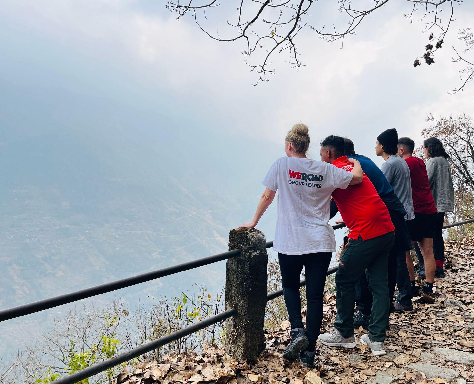 Eine WeRoad-Gruppenreise und ihr Reiseleiter stehen an einem Aussichtspunkt und blicken an einem bedeckten Tag über eine dunstige Bergkette.