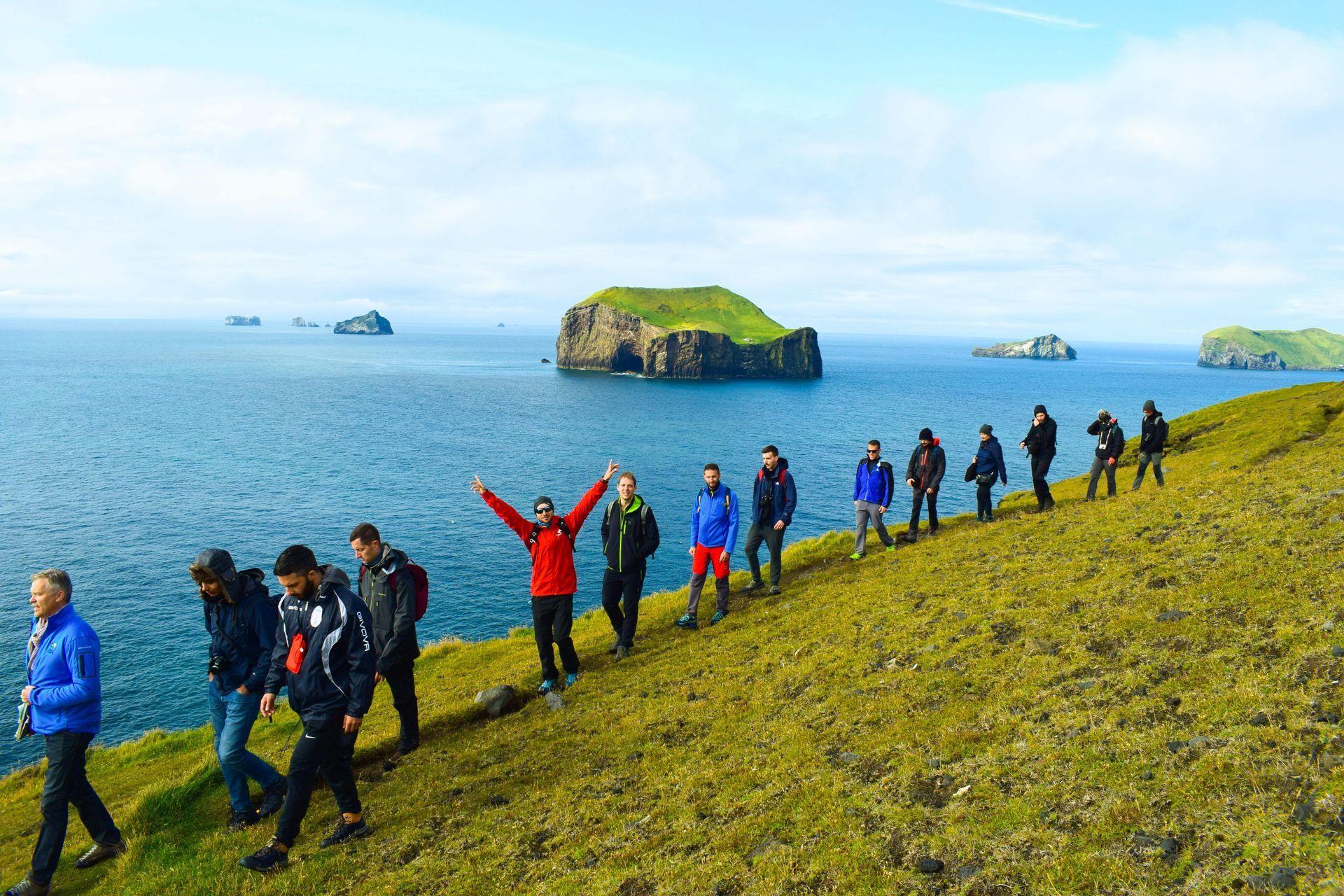 Un voyage de groupe WeRoad en randonnée sur une colline herbeuse surplombant un vaste océan bleu avec plusieurs petites îles rocheuses.