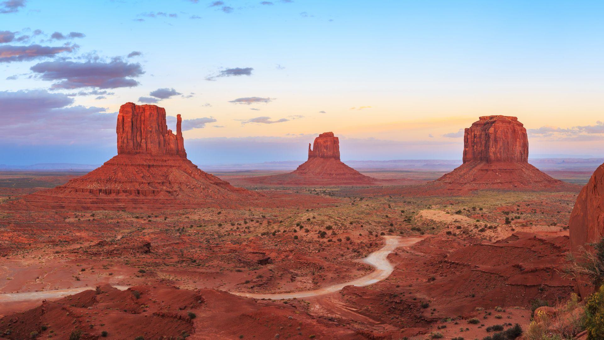 A prominent red sandstone butte rises from the desert floor under a sky with soft clouds at twilight.