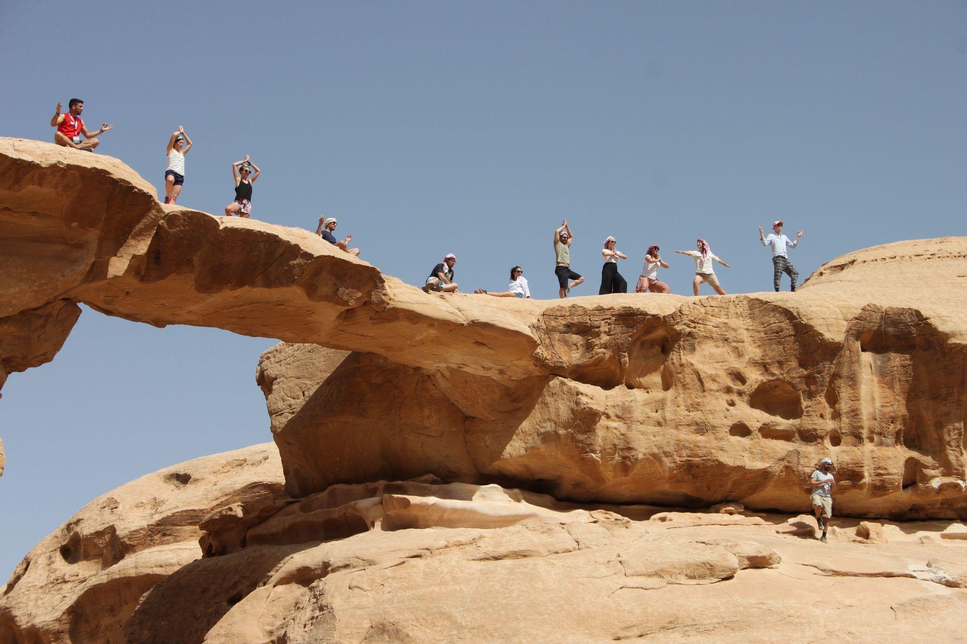 Un viaje en grupo de WeRoad posando para una foto en un gran arco natural de arenisca en el desierto.
