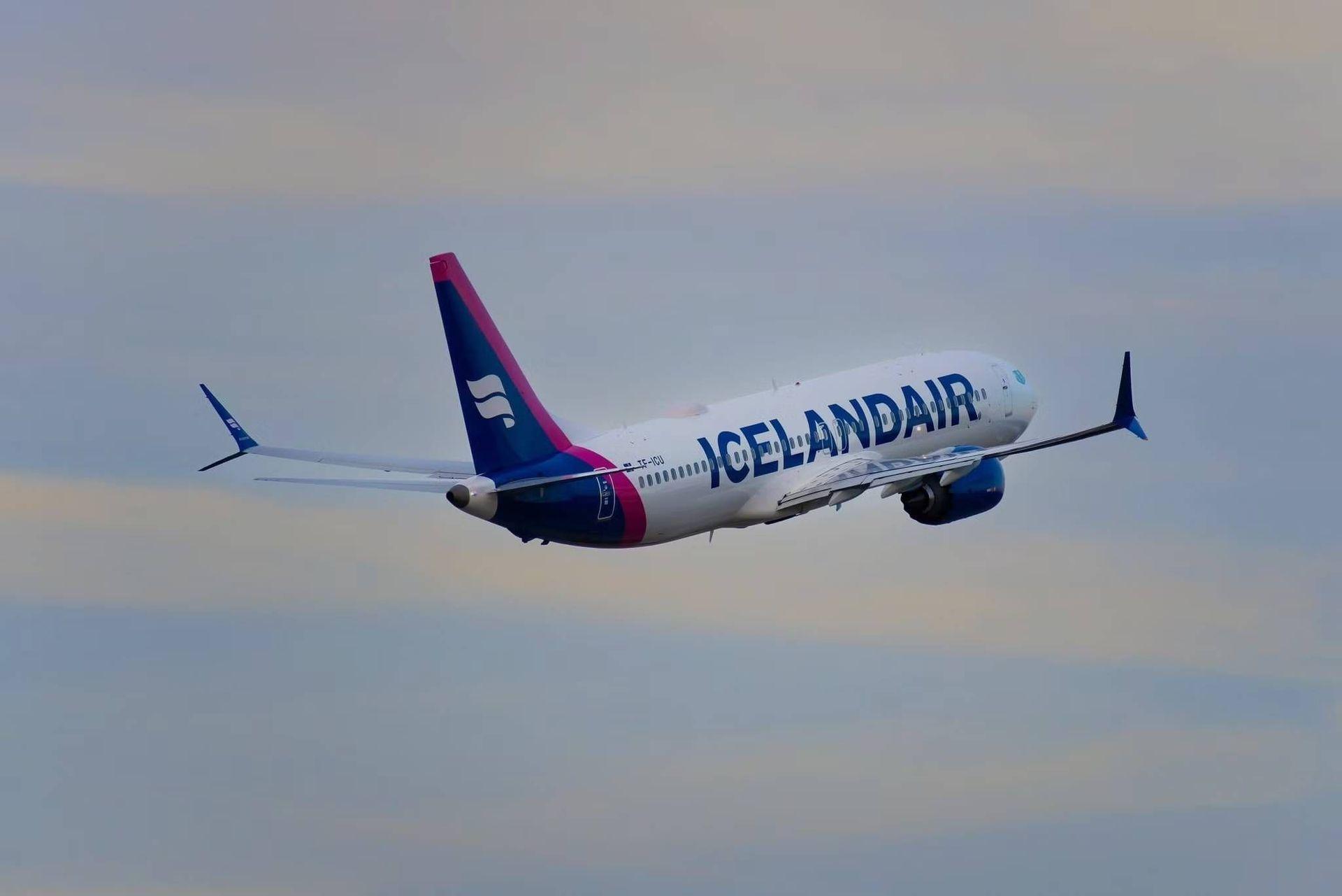 Un avión de Icelandair volando a través de un cielo parcialmente nublado, visto de lado.