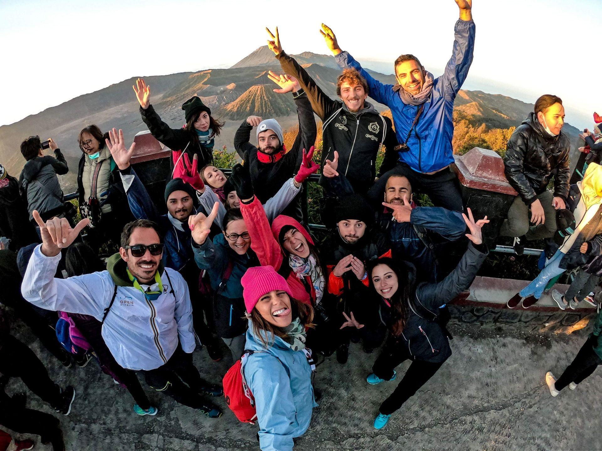 Un grupo de WeRoad posando para una selfie en un mirador, con un gran volcán visible de fondo al amanecer.