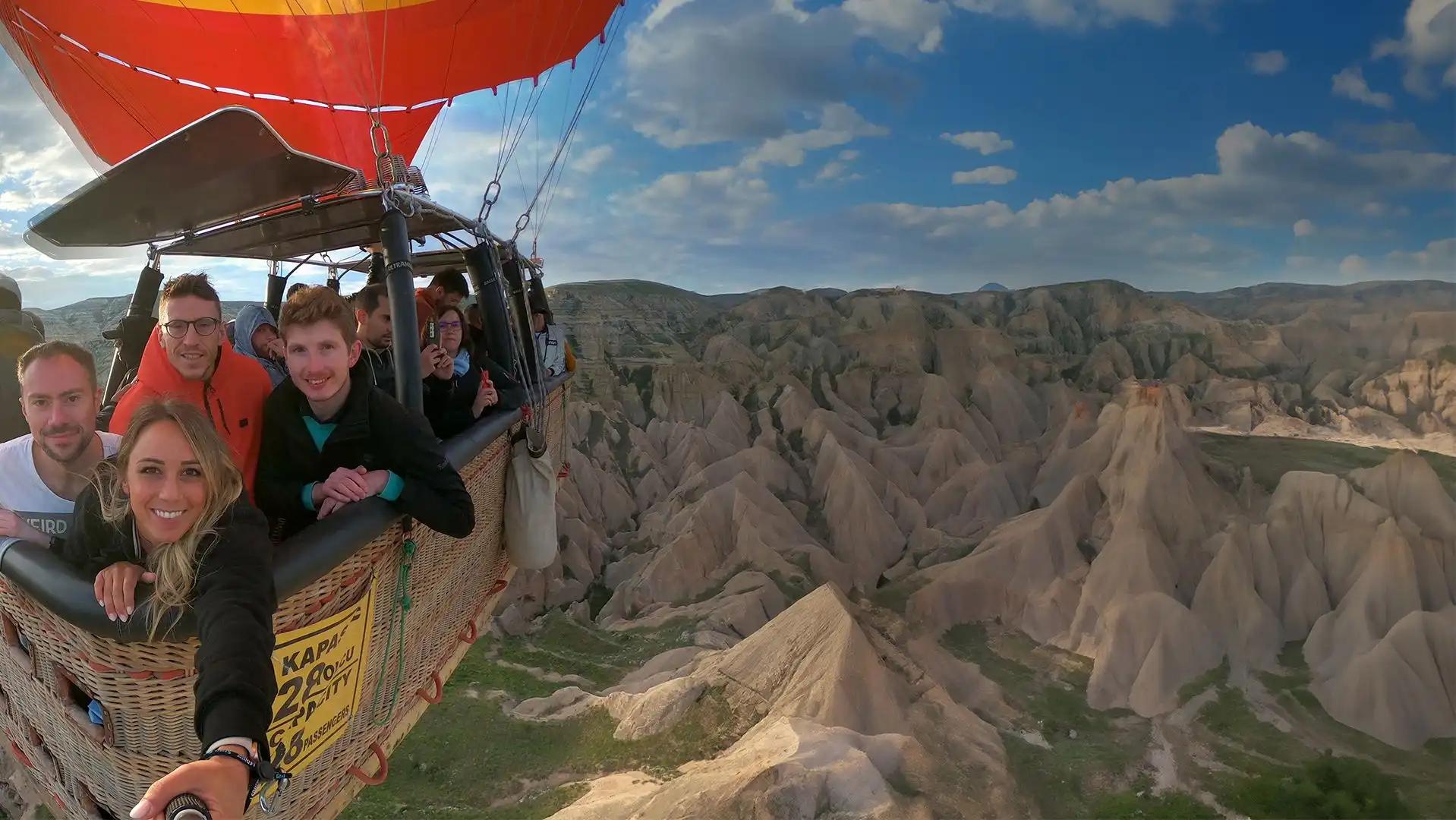 Diverse mongolfiere sono in un campo, in fase di gonfiaggio con i bruciatori accesi che brillano durante un'alba colorata, mentre le persone si radunano.