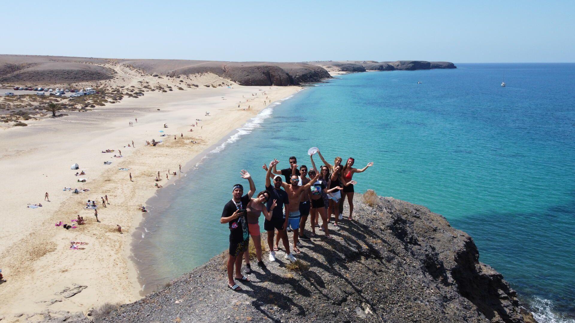 Un grupo de WeRoad posa y sonríe en un acantilado rocoso con vistas a una playa de arena y un océano turquesa.