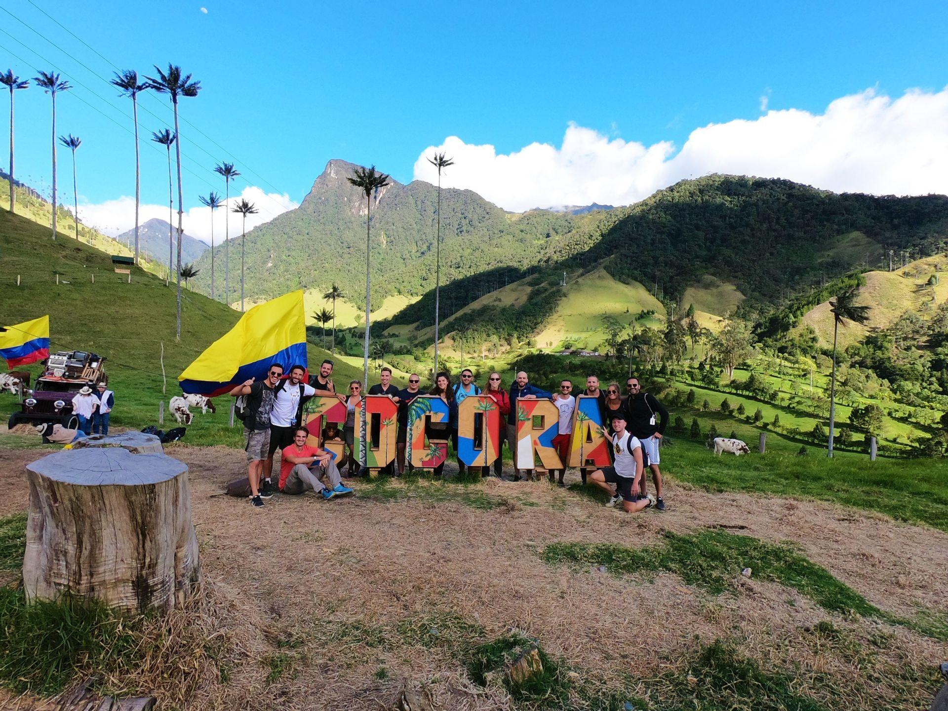 Un gruppo WeRoad in posa su una jeep rossa con una bandiera colombiana, con colline verdi e alte palme sullo sfondo.