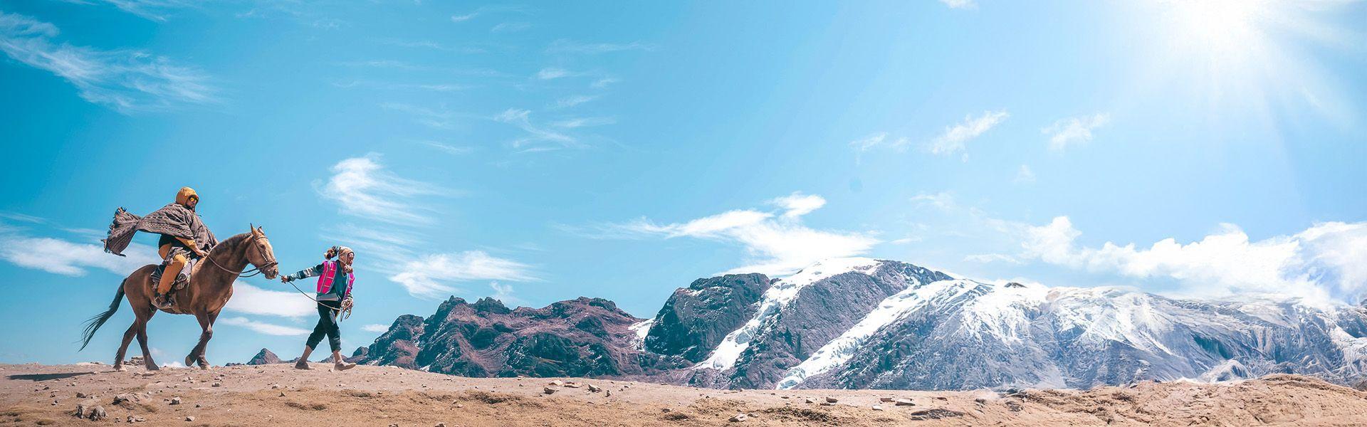 Una persona conduce un cavallo con un cavaliere di un viaggio di gruppo WeRoad attraverso un altopiano roccioso con montagne innevate.