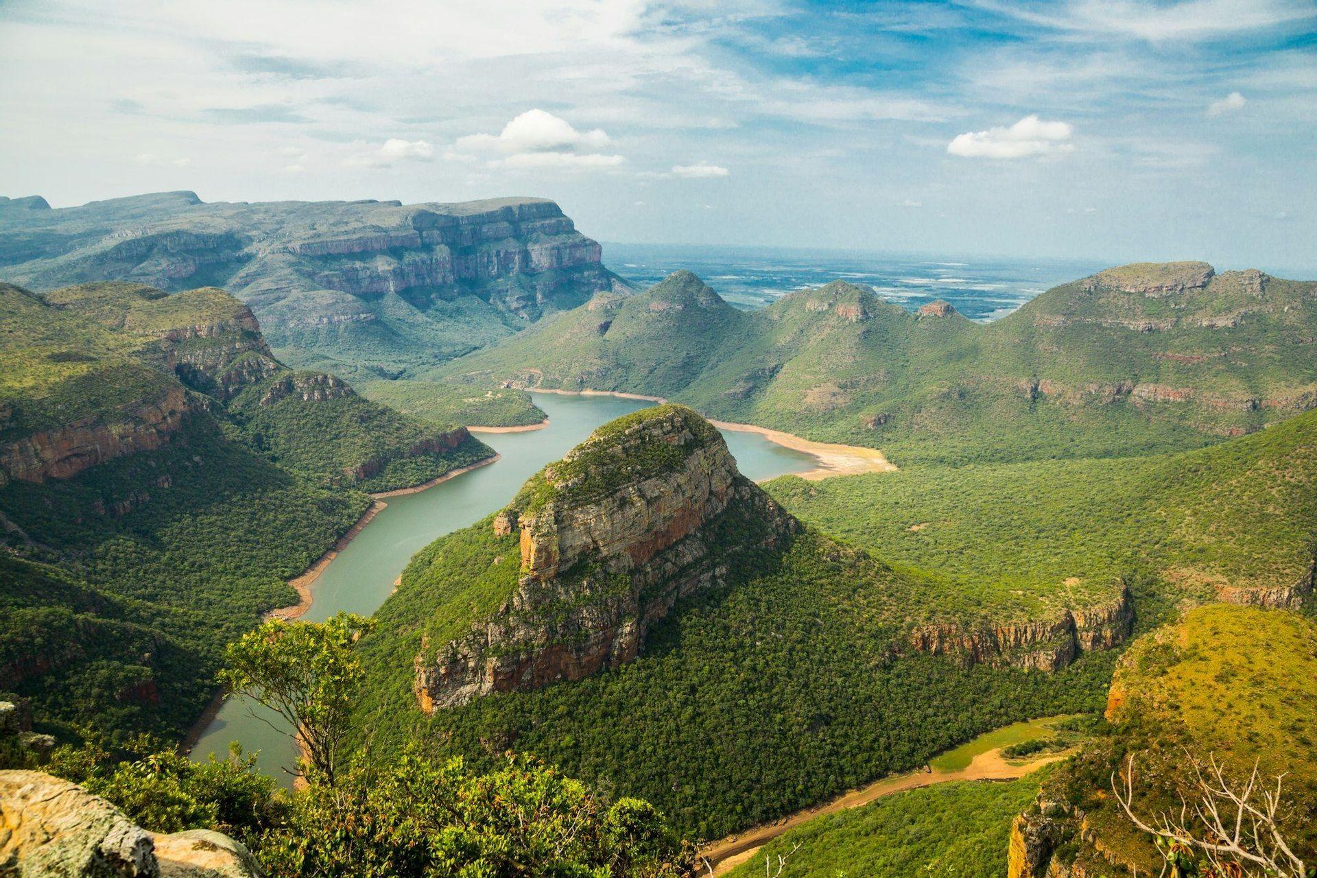 Un río ancho serpentea a través de un cañón profundo rodeado de exuberantes montañas verdes bajo un cielo azul con nubes dispersas.