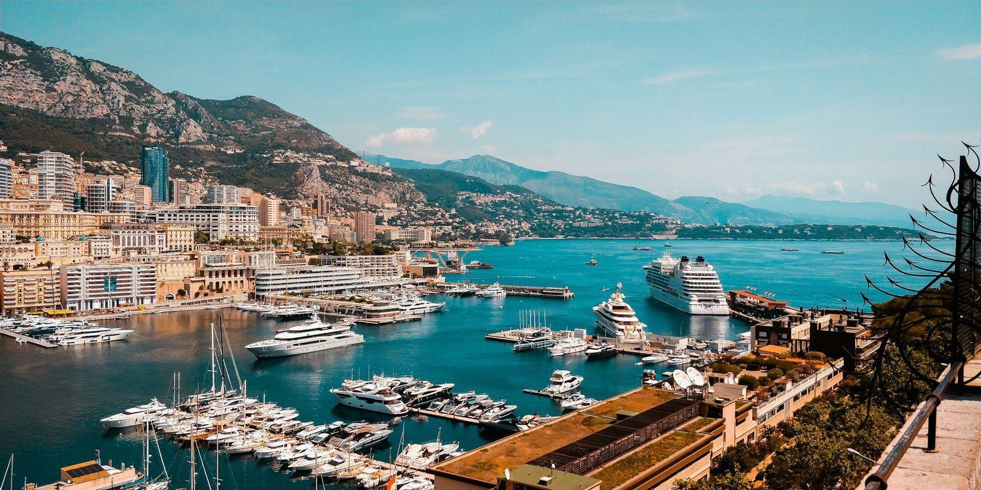 Una vista dall'alto di un porto colmo di yacht e navi da crociera, con una città costruita sulle pendici della montagna circostante sotto un cielo sereno.