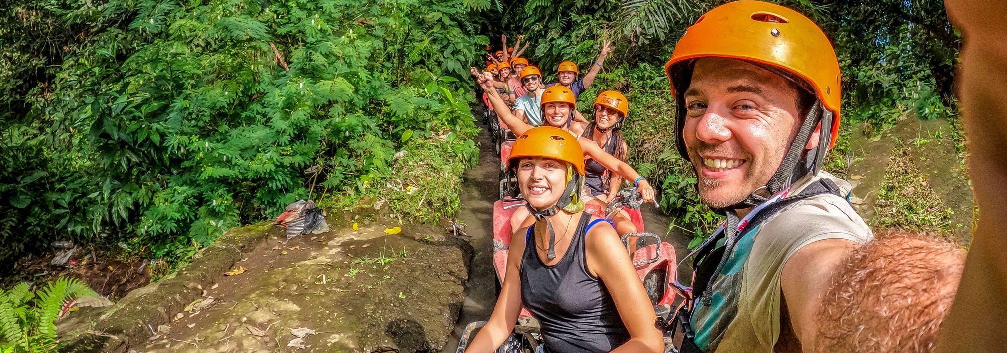 Un hombre se toma una selfie con su grupo de viaje de WeRoad mientras pasean en cuatrimotos en fila por un sendero fangoso en la jungla.