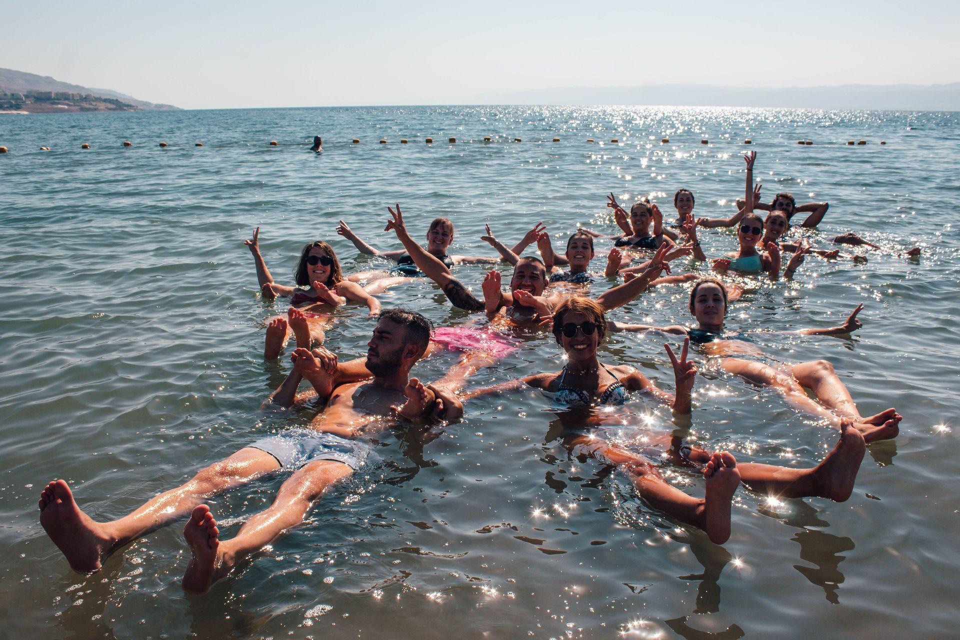 Viaja en grupo con WeRoad: descubre el mundo con gente de tu edad y con tus mismos gustos Foto de grupo bañándose en el mar muerto en Jordania