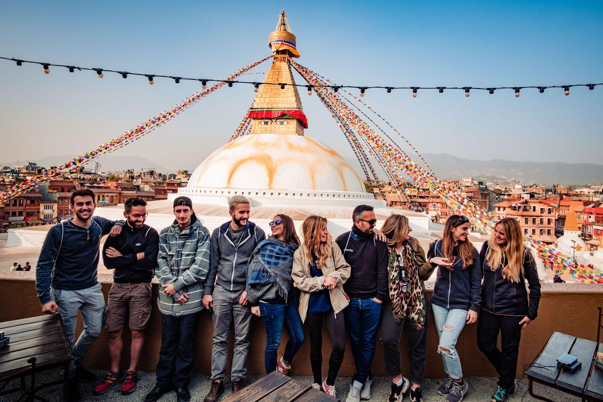 Un grupo de WeRoad posa para una foto en una terraza en la azotea frente a una gran estupa con banderas de oración coloridas.
