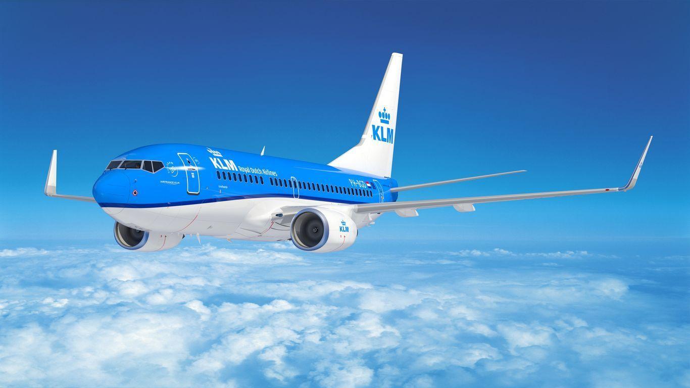 Un avión azul y blanco de KLM Royal Dutch Airlines volando sobre un mar de nubes bajo un cielo azul claro.