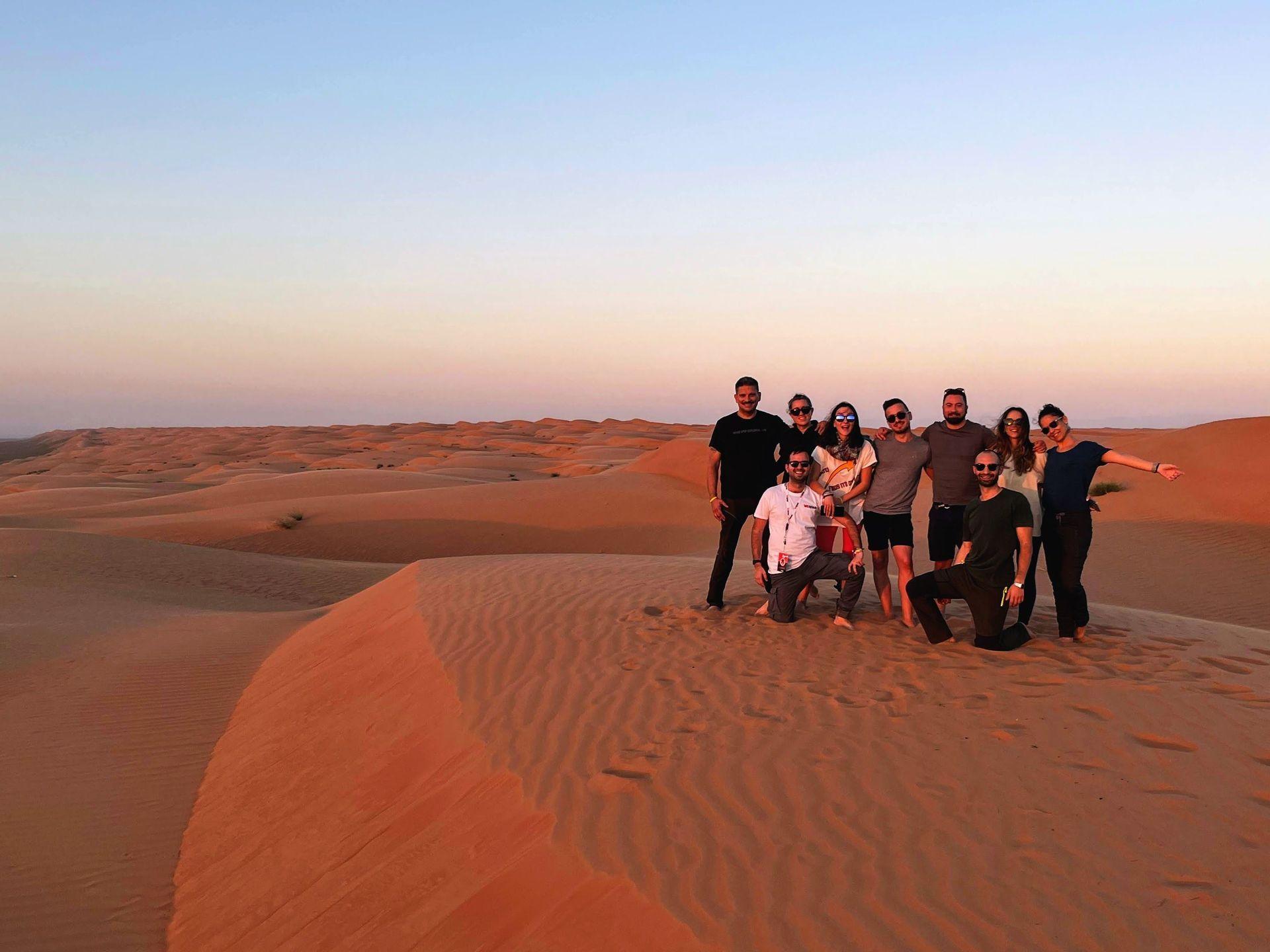 Un viaje en grupo de WeRoad posando para una foto en la cima de dunas de arena naranja durante el atardecer.