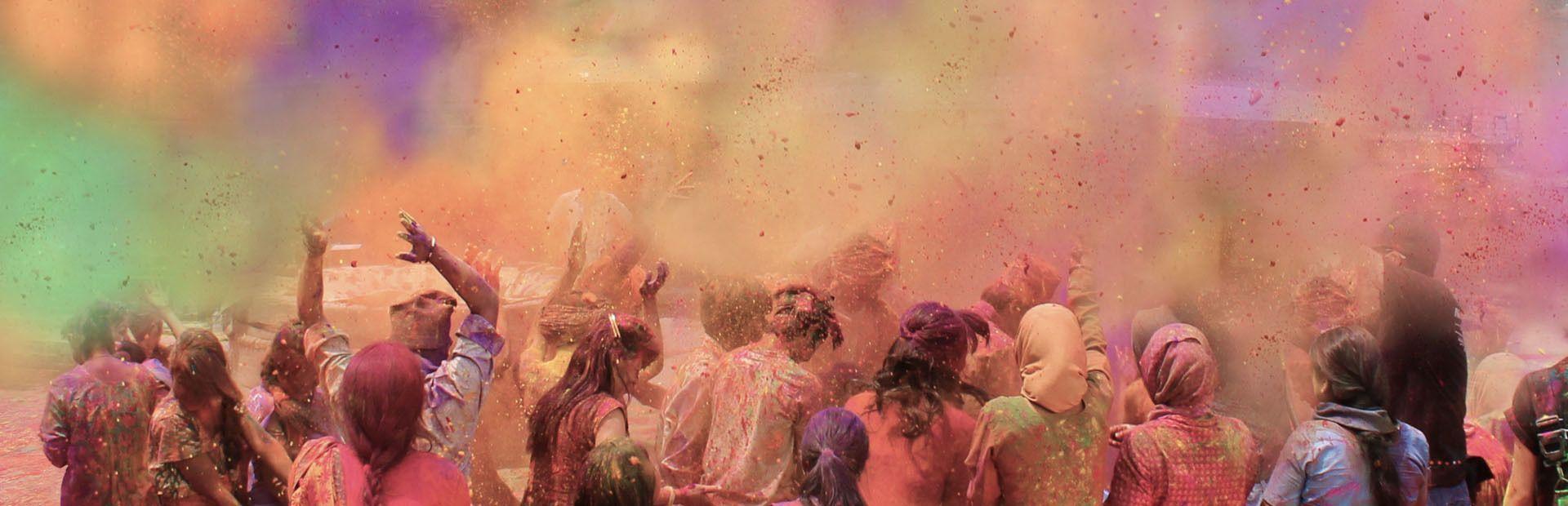 Un viaggio di gruppo WeRoad di persone viste di spalle che festeggiano il festival Holi lanciando polveri colorate in aria.