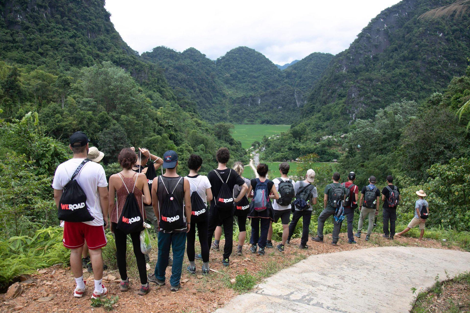 Un voyage en groupe WeRoad vu de dos, contemplant une vaste vallée verte entourée de montagnes.