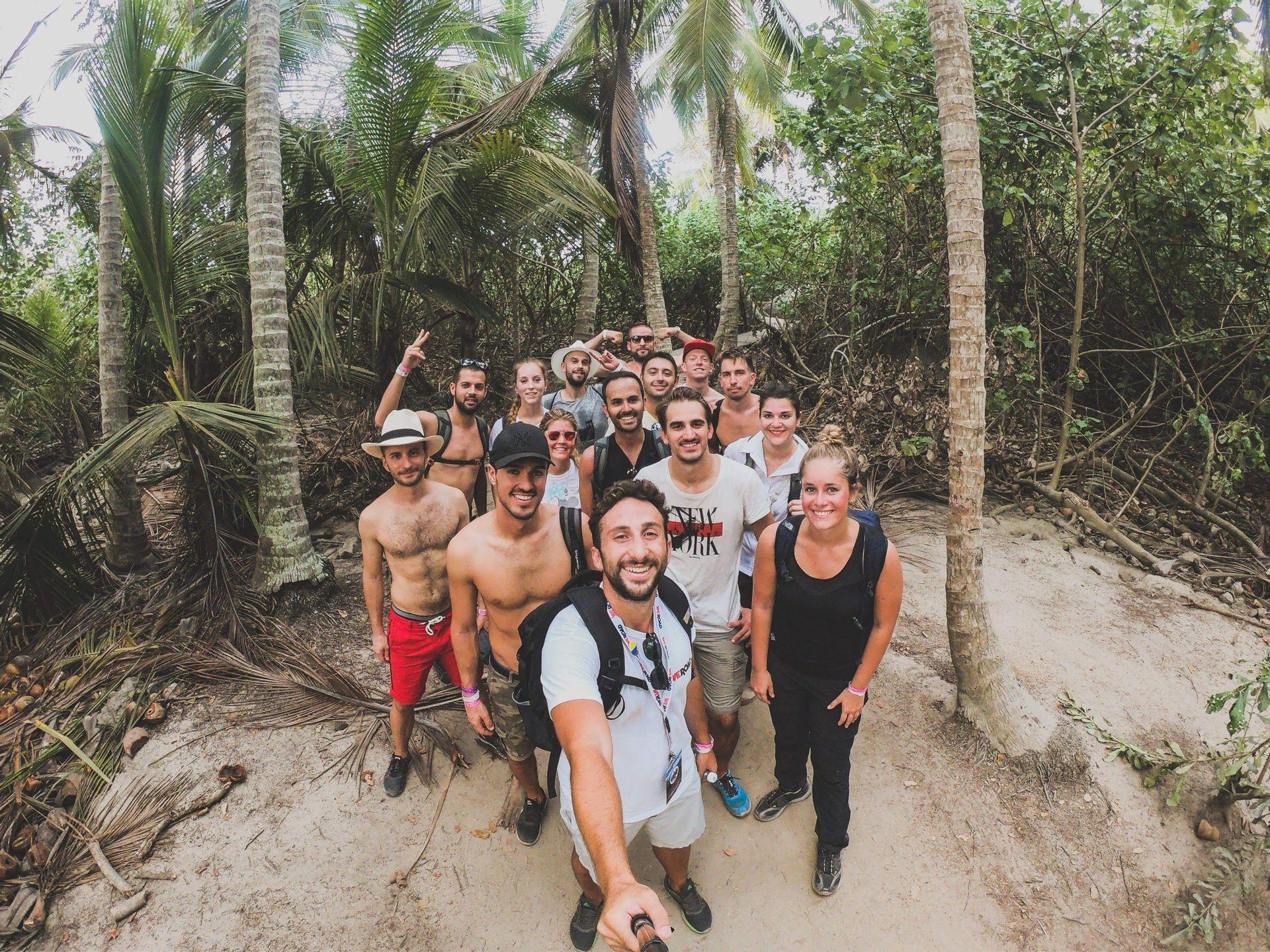 Un viaje en grupo de WeRoad se toma una selfie grupal en un sendero arenoso rodeado de altas palmeras y exuberante vegetación de la selva.