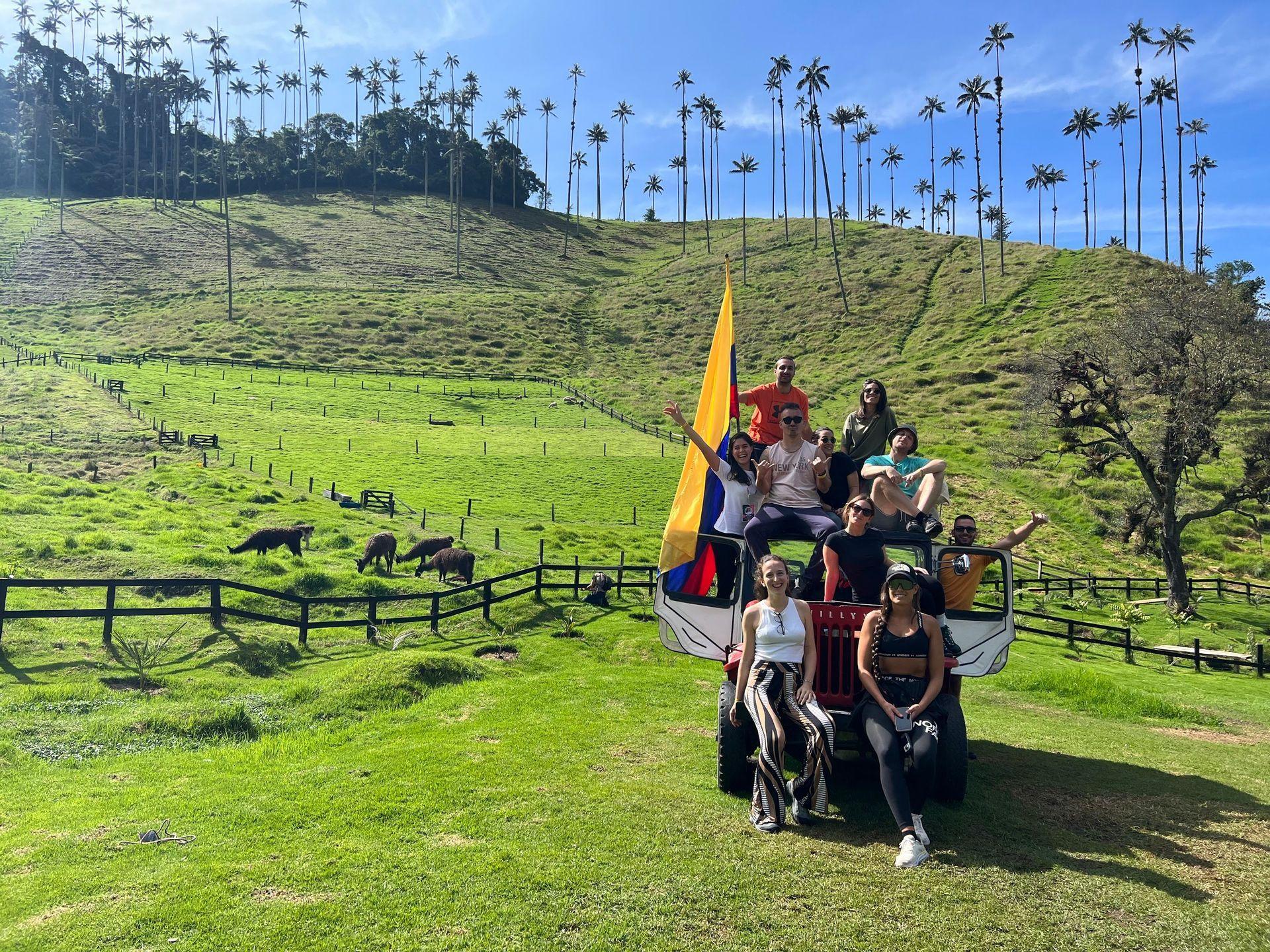 Un grupo de WeRoad posa en un vehículo todoterreno con una bandera colombiana en un paisaje verde montañoso con palmeras altas.