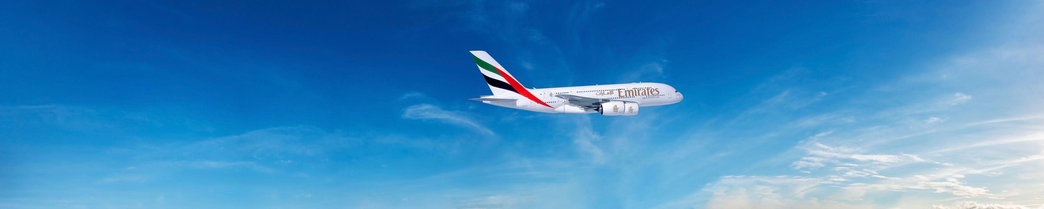 Un aereo passeggeri Emirates in volo attraverso un vasto cielo azzurro con nuvole bianche sparse.