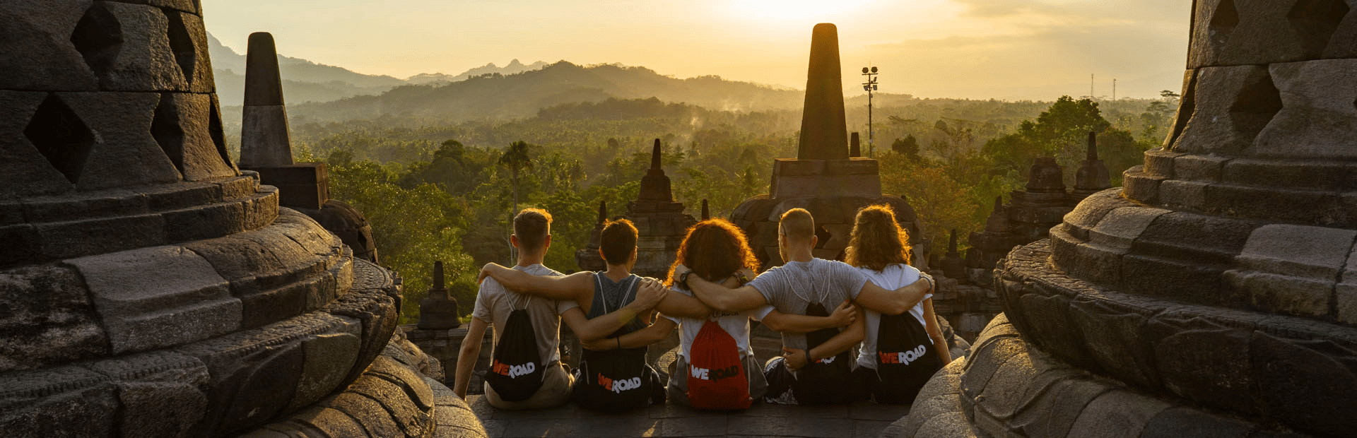 Un viaje en grupo de WeRoad observa el atardecer desde un templo de piedra con vistas a un valle montañoso y exuberante.