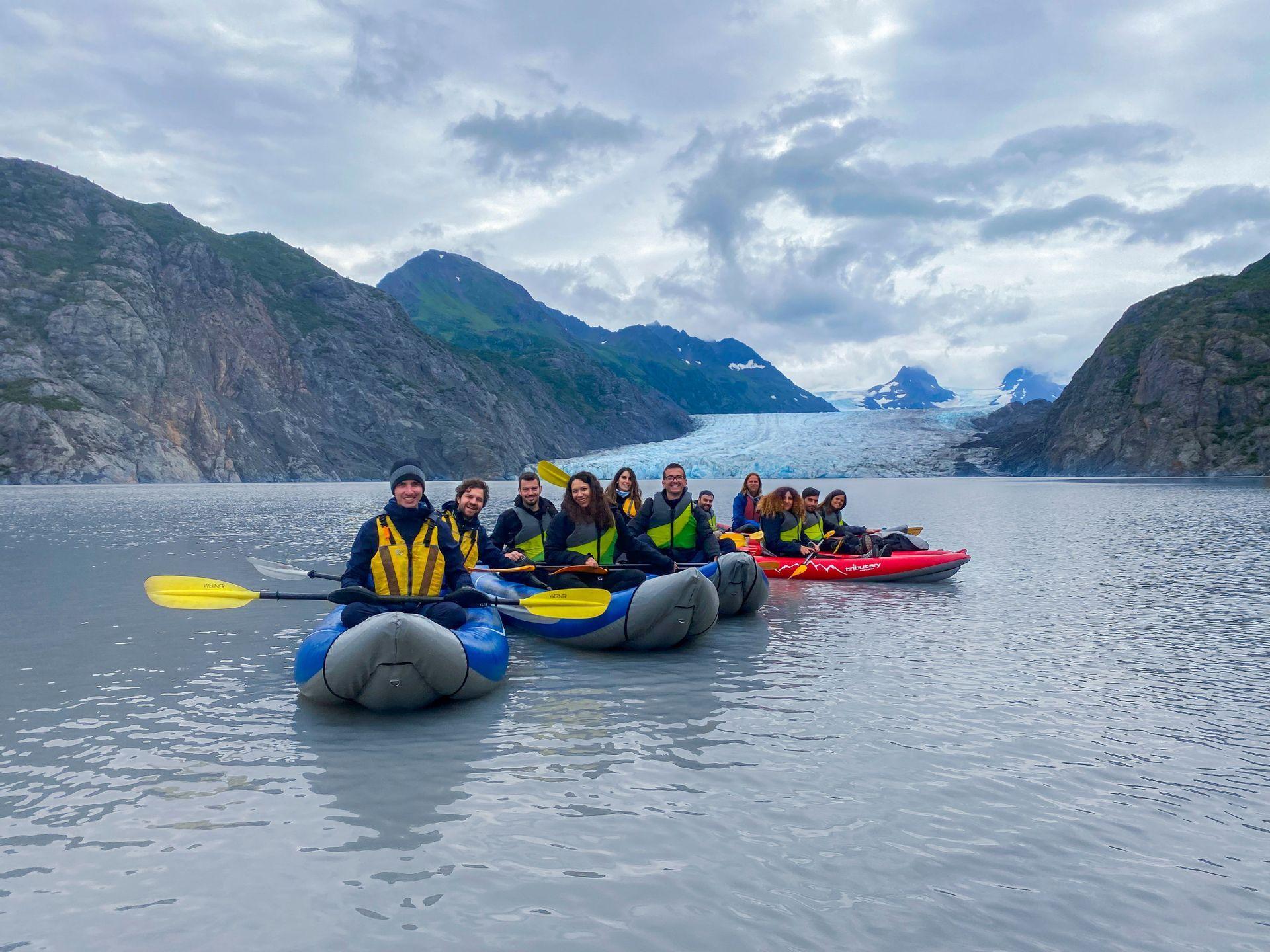 Viaje en grupo de WeRoad en kayak por un lago glacial, con un gran glaciar y montañas de fondo.