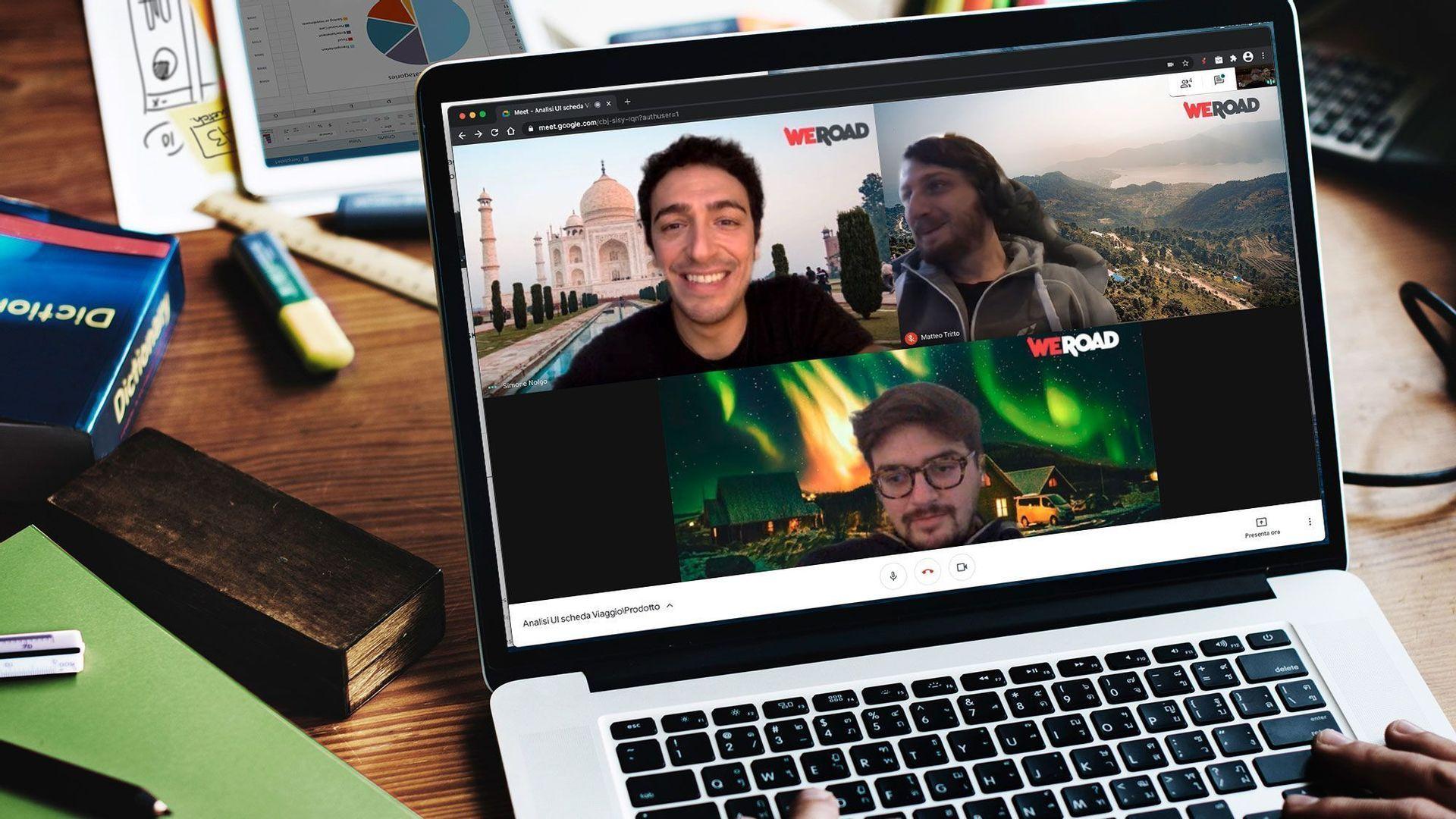 Un laptop su una scrivania mostra una videochiamata WeRoad con tre partecipanti che utilizzano sfondi virtuali a tema viaggio.