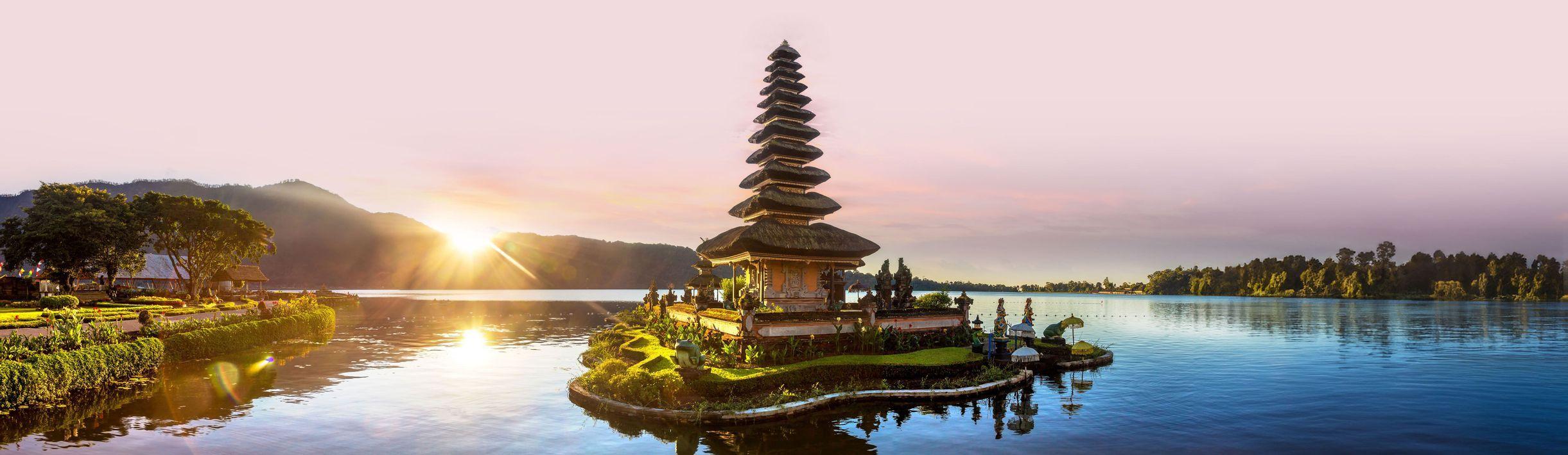 A multi-tiered temple on a small island in a calm lake at sunrise, with mountains in the distance and a colorful sky.