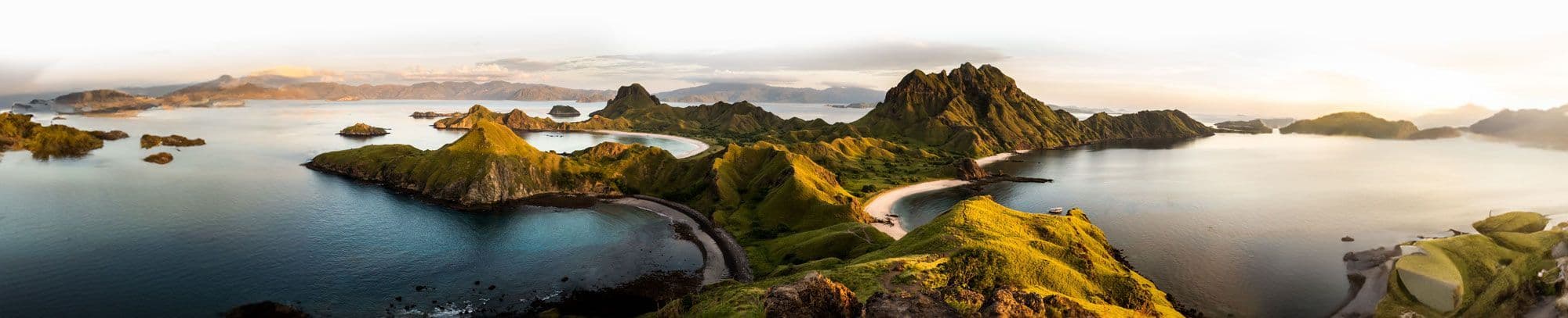 Una vista panorámica de un archipiélago con islas verdes escarpadas, calas con playas de arena blanca y aguas azules tranquilas.