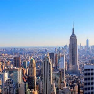 Ampia veduta aerea dello skyline di New York, con l'Empire State Building al centro, sotto un cielo limpido e azzurro.