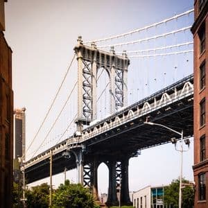 Un ponte sospeso in acciaio si erge tra due edifici in mattoni a più piani sotto un cielo sereno.