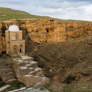 Un mausoleo di pietra con cupola bianca incastonato in una scogliera rocciosa, con ampie piattaforme e gradini in pietra in primo piano.