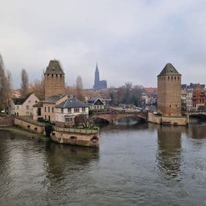 Torres de piedra y puentes arqueados cruzan un amplio río que atraviesa una ciudad histórica, con una catedral visible al fondo.