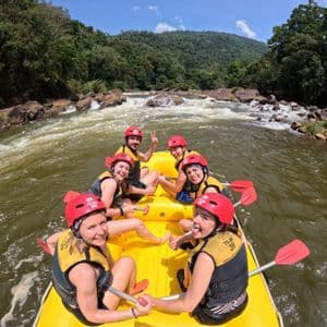 Eine WeRoad-Gruppe mit roten Helmen und Schwimmwesten lächelt während eines Rafting-Ausflugs auf einem gelben Schlauchboot für ein Foto.